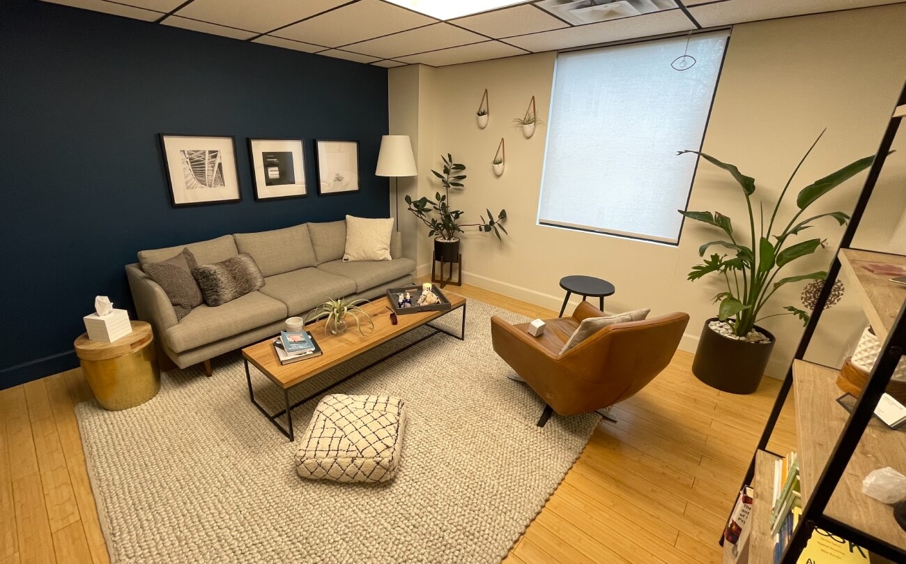 Calming room with a blue wall and plants, couch, and chair showing the patient treamtnet room in the clinic at K Therapy SLC.