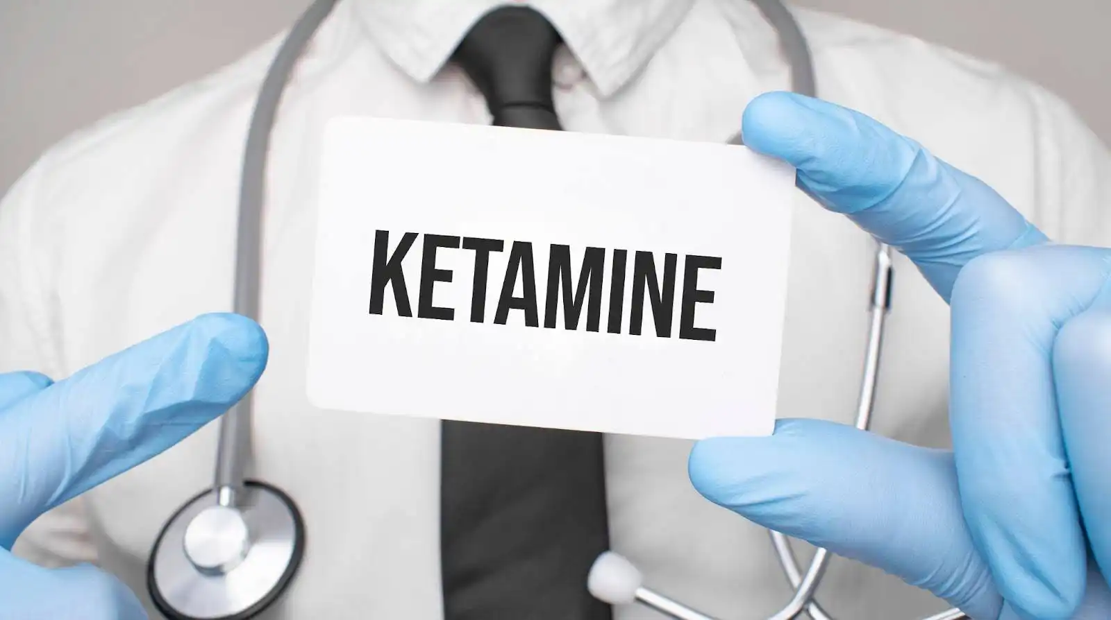 Gloved hands holding a card with the word ketamine on it symbolizing how Elon Musk advocates for Ketamine.