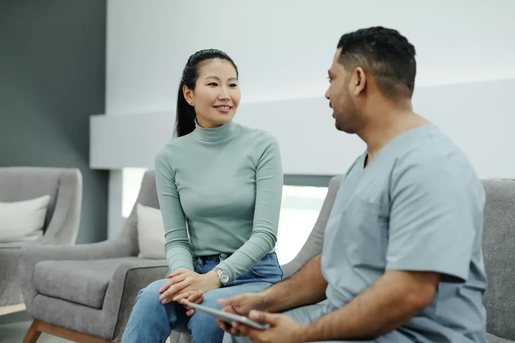 A patient and doctor are sitting on a grey couch talking about the differences between Ketamine vs Esketamine therapy.