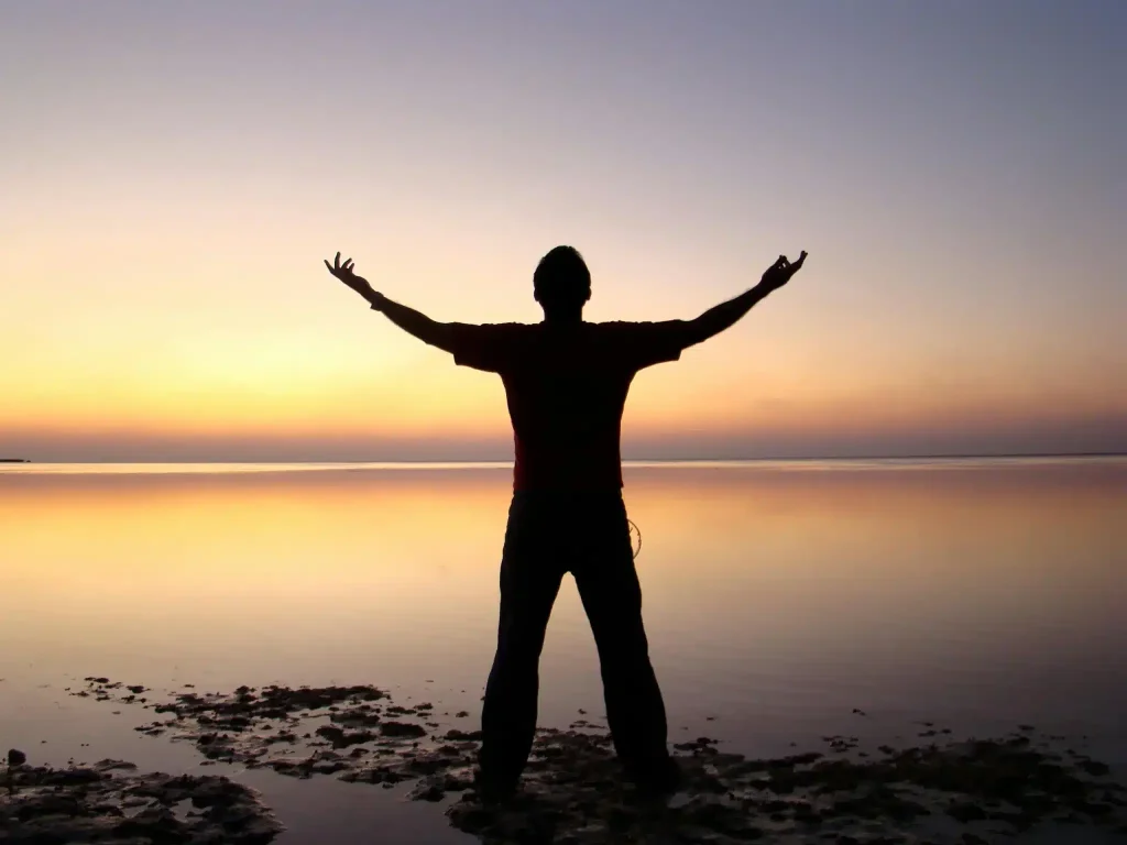 A person stands by the water at sunset after ketamine for gender dysphoria.
