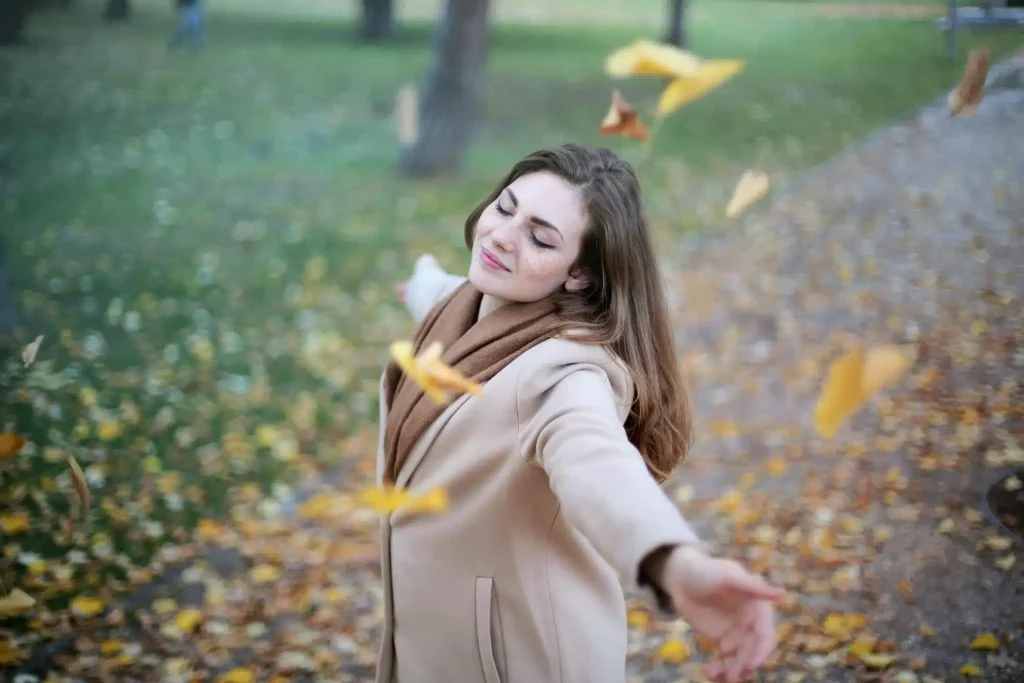 A woman in a beige coat stands in a park after feeling relief from ketamine for opioid withdrawal.